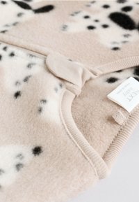 Puha bézs gyapjú anyag fekete és krémszínű foltokkal. Bordás szélén és patentos záródása van. Látható címke "Next Baby" márkázással.