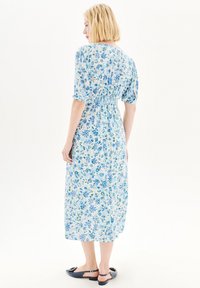 Robe maxi florale avec des motifs bleus et verts, manches courtes bouffantes et taille froncée. Tissu léger avec un design fluide.