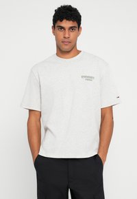 Grå bomulls-t-skjorte med korte ermer, med et grønt brodert logo på brystet. Casual passform med rund hals og minimalistisk design.