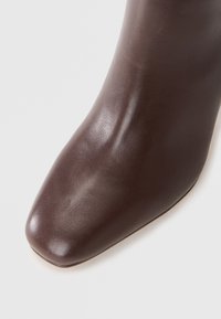 Hnědá kožená kotníková bota se čtveratou špičkou a hladkým povrchem, která se vyznačuje elegantním siluetou a jemným leskem na povrchu.