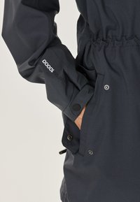 Marinblå vattentät jacka med elastiska muddar, justerbar midja och sidofickor. Har logodetalj på ärmen och tryckknappsstängningar.