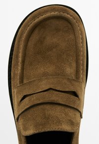 Mocassini in suede marrone con forma arrotondata, caratterizzati da un design a strati sulla tomaia e una suola nera a contrasto. Texture morbida e dettagli minimi.