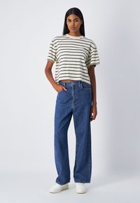 Camiseta corta de algodón a rayas con mangas cortas en crema y marrón oscuro. Jeans de pierna ancha de cintura alta en azul y zapatillas blancas.