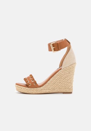 Wedge sandaal met een tan leren band, gevlochten touwhiel en een gestreepte stoffen accent aan de achterkant. Bevat gouden oogjes detail.