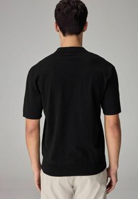 Sort kortærmet polo-shirt med struktureret overflade, der har en flad krave og ribbede manchetter, i et rent, minimalistisk design.