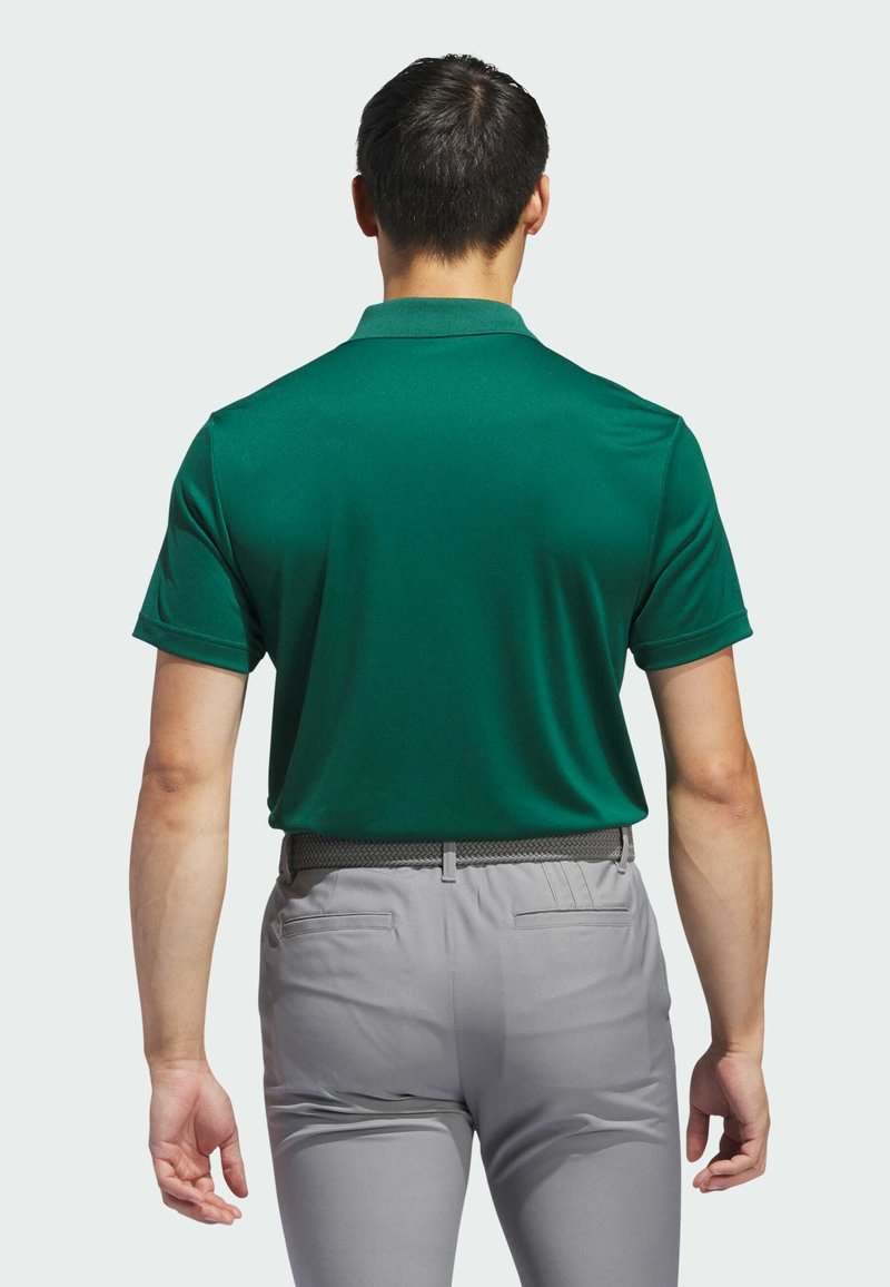 Grünes Poloshirt mit glatter Textur, kurzen Ärmeln und Kragen, kombiniert mit hellgrauen Hosen, die einen gewebten Gürtel und seitliche Taschen haben.