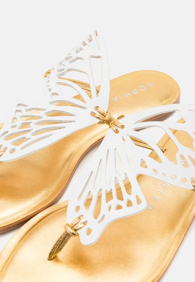 Conception de papillon blanc sur des sandales plates dorées, comportant des découpes, une finition métallique brillante et un logo simple sur la semelle intérieure.