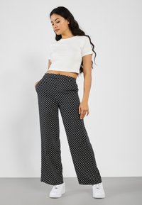 Black polka dot wide-leg pants with a high elastic waistband, paired with a fitted white cropped top and white sneakers.