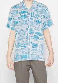 Koszula z krótkim rękawem w jasnoniebieskim kolorze na białym tle, z różnymi nadrukowanymi wzorami, tekstem i kołnierzykiem zapinanym na guziki.