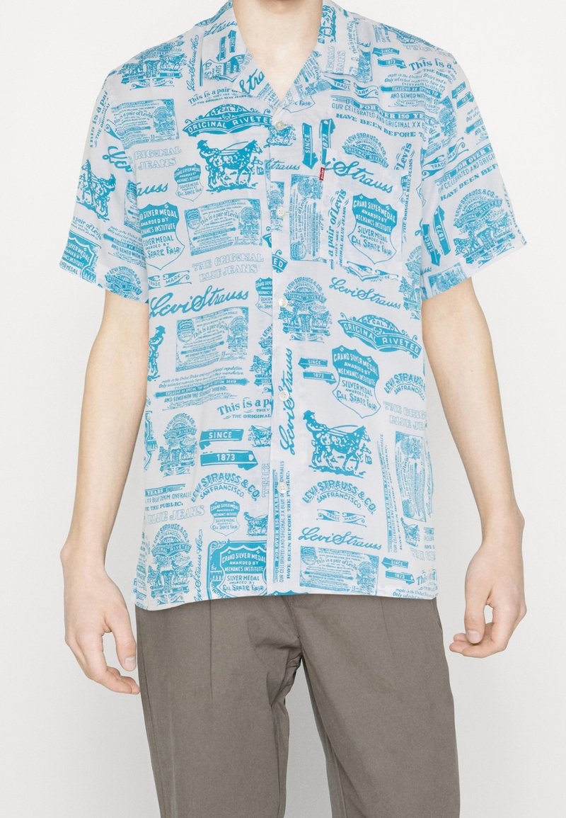 Koszula z krótkim rękawem w jasnoniebieskim kolorze na białym tle, z różnymi nadrukowanymi wzorami, tekstem i kołnierzykiem zapinanym na guziki.