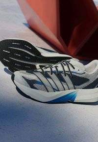 Sive atletske tenisice s gornjim dijelom od mrežice, crnim i plavim naglascima, teksturiranim potplatom i istaknutim natpisom „LIGHTSTRIKE" sa strane.