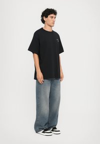Svart bomulls t-skjorte med korte ermer og rund hals, kombinert med løstsittende, falmede blå jeans og svarte og hvite joggesko.