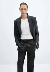 Šedý dobře padnoucí blazer přes bílý upnutý top, doplněný černými koženými tepláky se stahovací páskou.