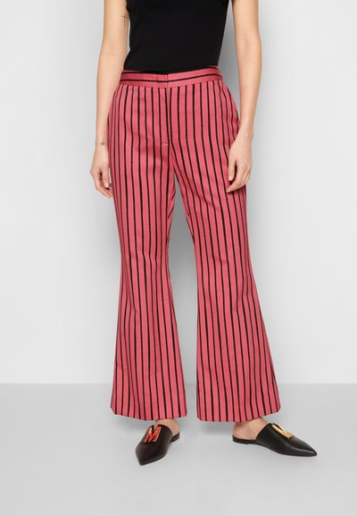 Calças largas rosas com riscas verticais pretas, cintura alta e uma textura suave. Combinadas com mules pretas pontiagudas com um detalhe decorativo.