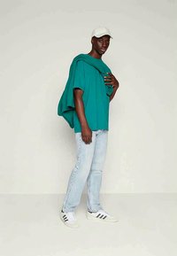 Teal oversized skjorta med korta ärmar, kombinerad med ljusblå slitna jeans och vita sneakers med svarta ränder.