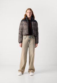 Kuttet boblejakke i svart med leopardmønster, parret med lyse, løs passform jeans og hvite joggesko.