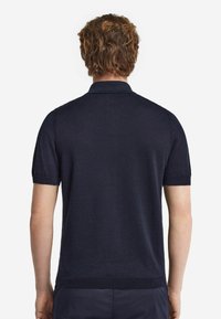 Marinblå kortärmad polo med krage, sömlös textur, ribbade muddar och fåll samt en ren, modern passform.