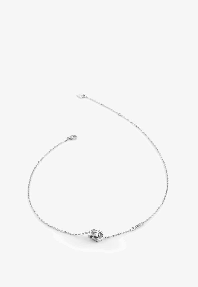 Zilveren schakelarmband met een hartvormige hanger met een kleine edelsteen en een sluiting, gemarkeerd met de merknaam "Guess."