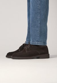 Braune Wildlederschuhe mit runder Spitze, Schnürdesign und texturierter Oberfläche, kombiniert mit hellblauen Jeans.