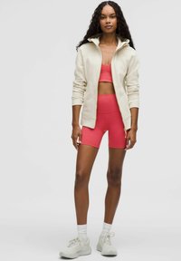 Bijela jakna na zip, ružičasti skraćeni top i odgovarajuće šorceve s visokim strukom. Teksturirani materijal, sportskog kroja i lagane tenisice.