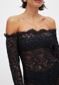 Must musta õla alt avatud pitskleit lillemuster ja sädelevate detailidega. Tekstuuriga kangas pikkade varrukate ja laineliste äärtega.