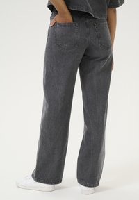 High-waisted, wide-leg jeans in a dark gray denim. Features include two back pockets and a slight texture, paired with white sneakers.