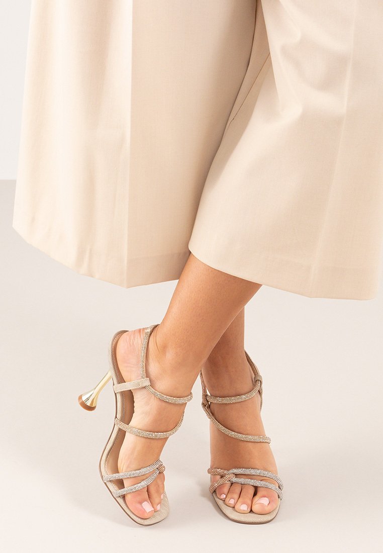 Sandalias de tacón beige con múltiples correas adornadas con strass. Diseño de punta abierta con un elegante tacón metálico.