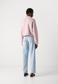 Rosa strikket genser med en kort design, kombinert med lyseblå høytaltes jeans. Modellen har på seg svarte blokkhevede sandaler.