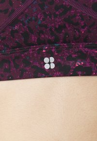 Αθλητικό σουτιέν με πολύχρωμο μοτίβο ζώου σε αποχρώσεις του μωβ και του μαύρου, διαθέτοντας λεία υφή και μια μικρή ανακλαστική λεπτομέρεια λογότυπου.