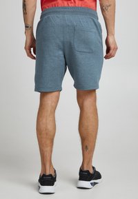Grå sweatshorts med snøre i taljen, med en baglomme og opviklede kanter, kombineret med mørke sportssko.