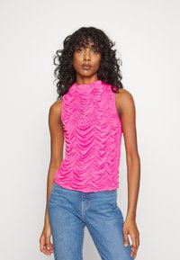 Top sem mangas fúcsia com um decote alto, apresentando um design texturizado e franzido. Usado com jeans de ganga azuis.