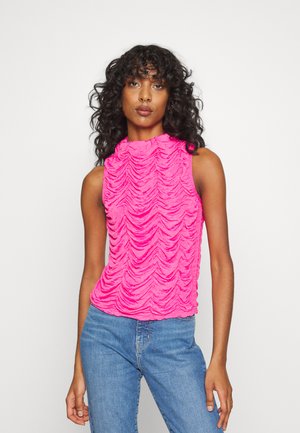 Top sem mangas fúcsia com um decote alto, apresentando um design texturizado e franzido. Usado com jeans de ganga azuis.
