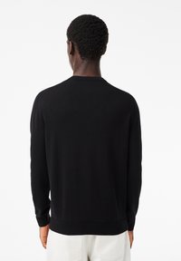 Maglione nero con scollo rotondo, polsini e orlo a coste. Presenta una texture liscia e un design aderente, visto da dietro.