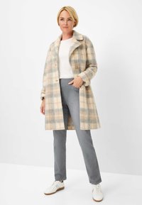 Manteau long à carreaux beige et bleu clair, en mélange de laine, avec de grands revers et deux boutons. Associe à un pantalon gris et des baskets blanches.