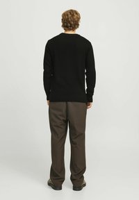 Schwarzer gestrickter Pullover mit einem strukturierten Muster, Rundhalsausschnitt und gerippten Bündchen, kombiniert mit braunen Hosen und schwarzem Schuhwerk.