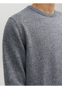 Pull gris en maille avec une finition texturée. Col rond avec un motif chiné subtil. Tissu lisse et coupe décontractée.