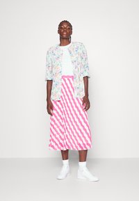 Camisa de botão com estampa floral, t-shirt branca e saia midi com padrão zigzag rosa. Complementada com ténis brancos e meias até ao tornozelo.