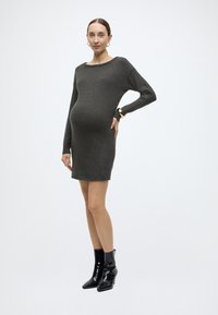 Γκρι πλεκτό φόρεμα εγκυμοσύνης με μακριά μανίκια και λαιμόκοψη τύπου βάρκα, συνδυασμένο με μαύρα μποτάκια αστραγάλου από δέρμα lak. Λείο υλικό και εφαρμοστή σιλουέτα.