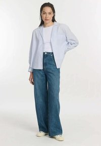 Lichtblauwe gestreepte button-up shirt over een wit topje, gecombineerd met hoge wijdvallende blauwe jeans en witte sneakers.