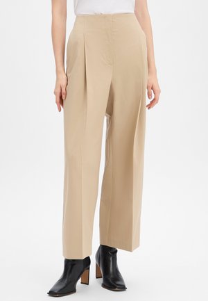 Pantaloni beige a gamba larga con pieghe frontali, realizzati in un morbido tessuto misto cotone. Abbinati a stivaletti neri con tacco.