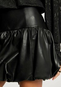 Gonna nera in ecopelle con vita aderente e orlo arricciato, caratterizzata da una texture liscia e una silhouette voluminosa.