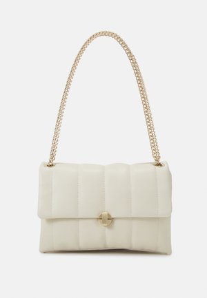 Kremowa pikowana skórzana torebka na ramię z złotym okrągłym zapięciem i masywnym złotym łańcuchem na tle białym.