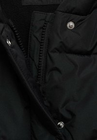 Tissu d'une doudoune noire avec une texture matelassée ; comprend une fermeture éclair argentée, un bouton-pression et une doublure intérieure douce.