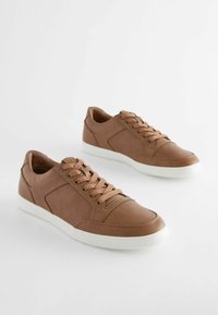 Bruna lädersneakers med perforerade sidodetaljer, platta snören och vita gummisulor. Rundad tådesign. Slät textur.