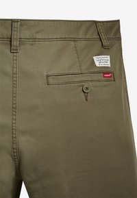 Pantalon vert olive avec une texture lisse, comprenant une poche arrière avec un bouton et une étiquette de la marque Levi's cousue au-dessus.