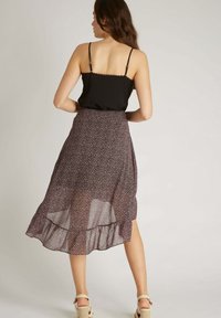 Camisole noir à fines bretelles, associé à une jupe fluide avec un imprimé floral sur un tissu sombre, présente un ourlet à volants, arrive au-dessus des chevilles.