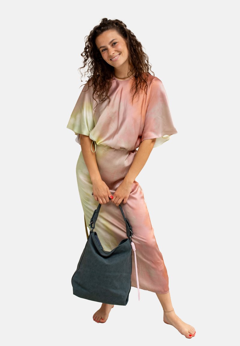 Abito fluido in gradiente rosa e verde con maniche corte. La modella tiene una grande borsa grigia scura con tracolla regolabile e dettagli rosa.