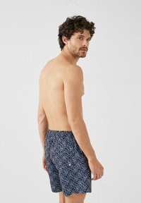 Shorts de baño azules con un estampado geométrico blanco y una cinturilla elástica; están hechos de un tejido ligero.