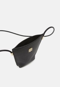 Mała czarna skórzana torebka na ramię z cienkim paskiem i złotym logo na przodzie, przedstawiona otwarta na białym tle.