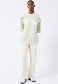 Light green oversized t-shirt with white text "AROUND THE WORLD" on front, paired with off-white wide-leg pants and gray sneakers.